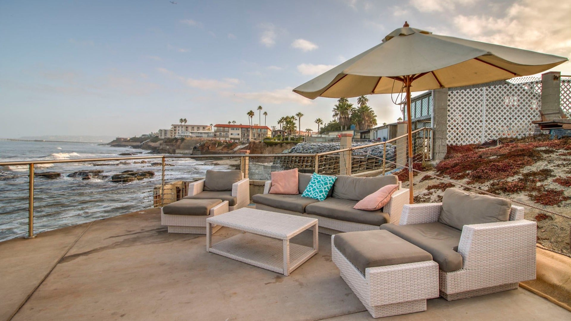 seating area with umbrella overlooking the ocean, view of hotels and trees at the back